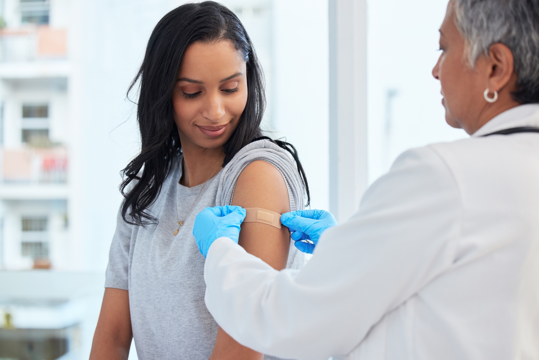 Urgent care professional putting bandaid on woman's upper arm where she got a flu shot