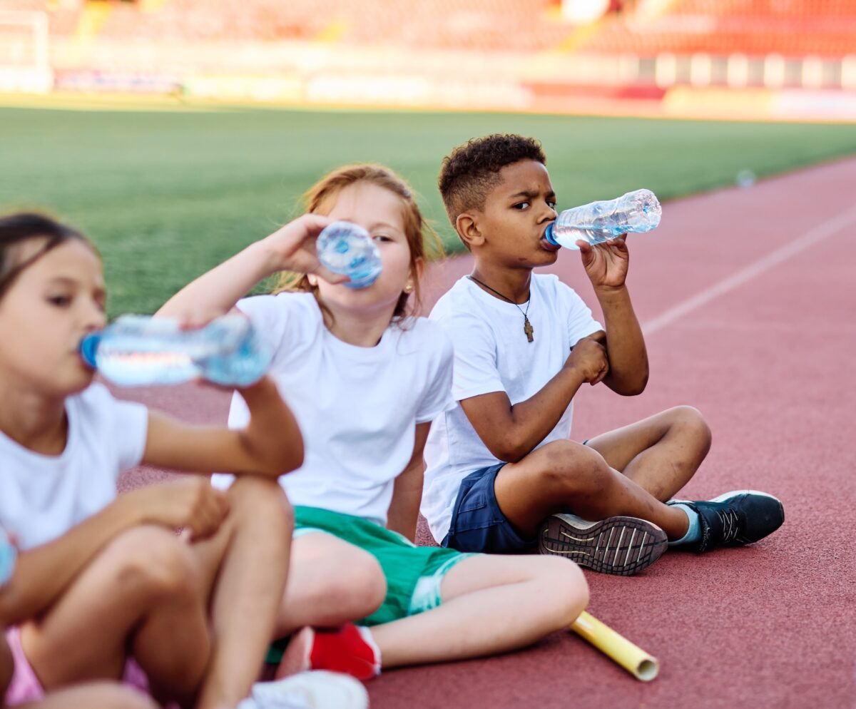 Children resting and drinking water after running on a track at their school stadium