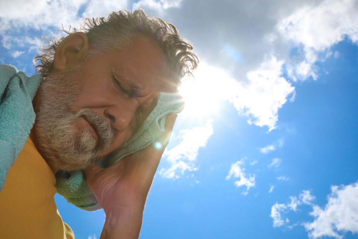 Older man holding a towel to his forehead, tired from the summer heat